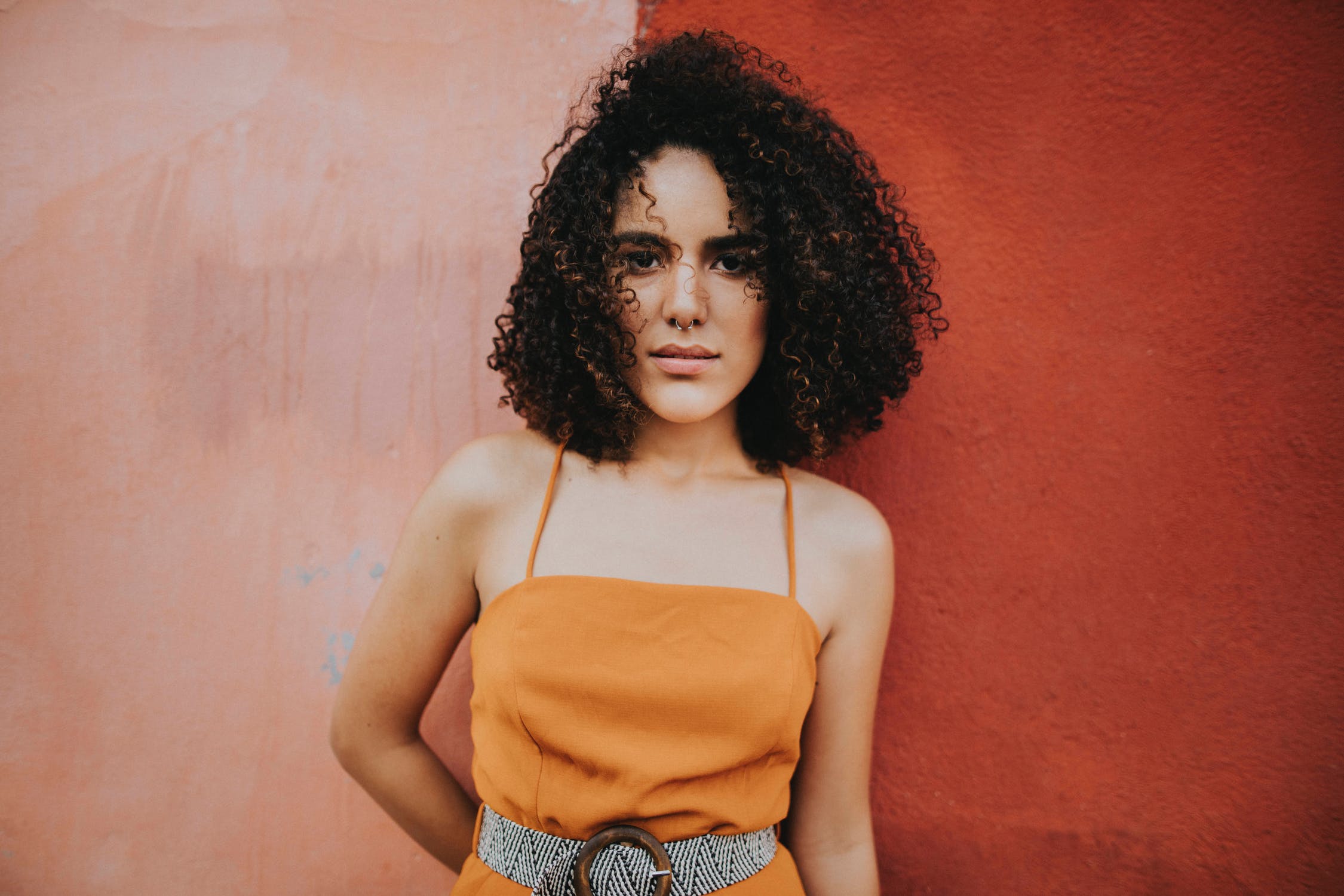 Female with luscious curly hair standing against a red and pink background